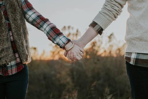 Two people hold hands while outside.