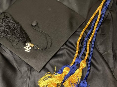 A graduation cap and gown adorned with honors accolade cords.